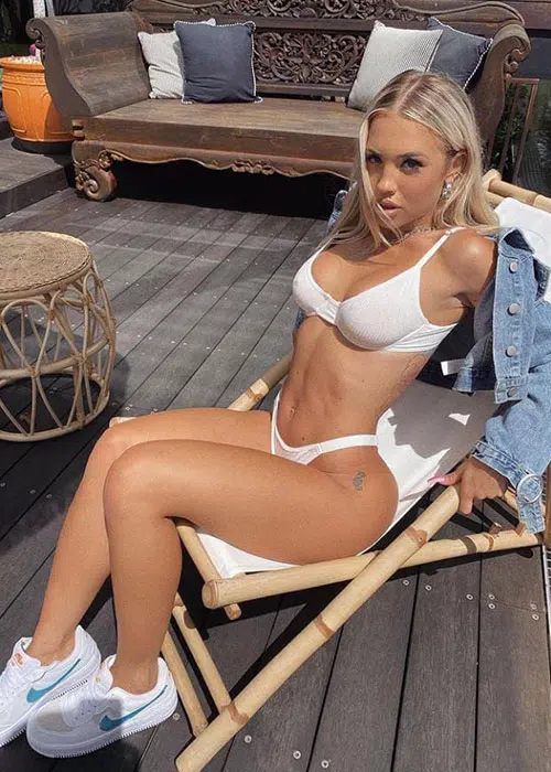 Blonde woman in white thong and panties pushes herself up from a pool chair.