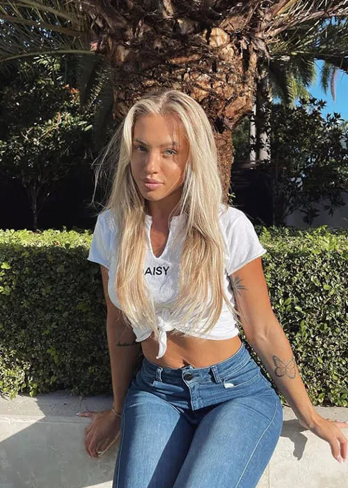 Blonde woman sits under California sun wearing blue jeans and cut-off white t-shirt.